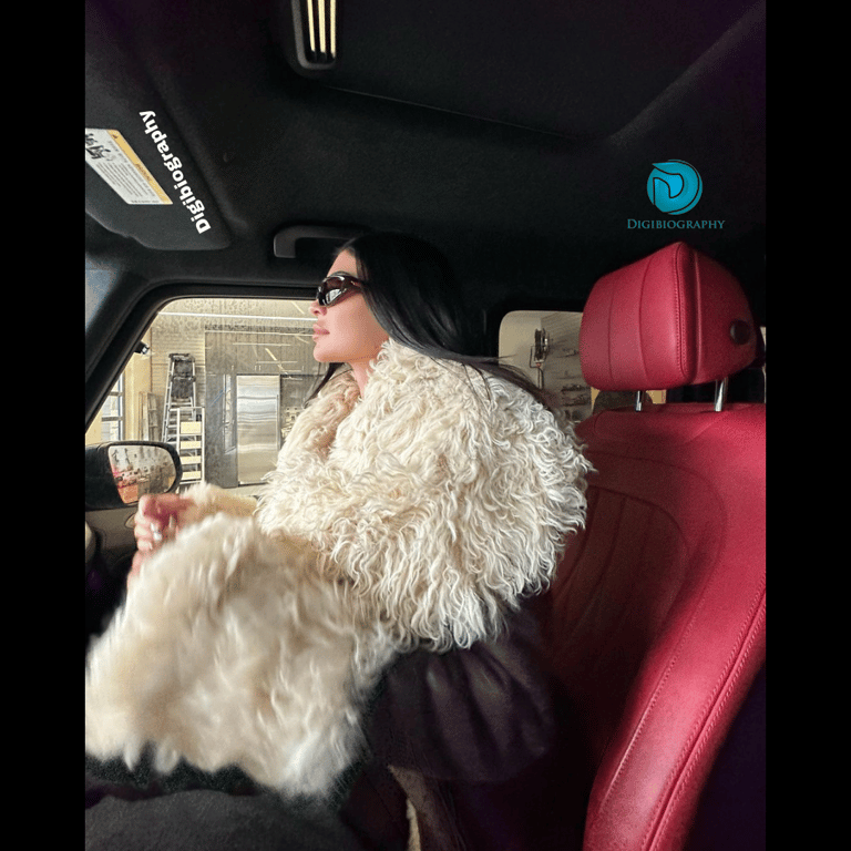 Kylie Jenner wearing a fur jacket and sitting in front of the car