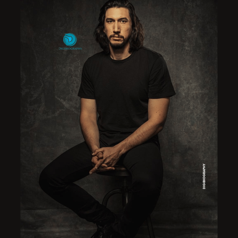 Adam Driver sitting on the chair and wearing a black t-shirt and black jeans