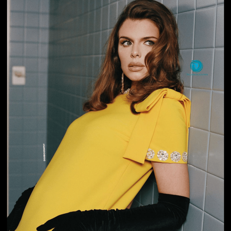 Julia Fox stands close to the wall and wears a yellow dress