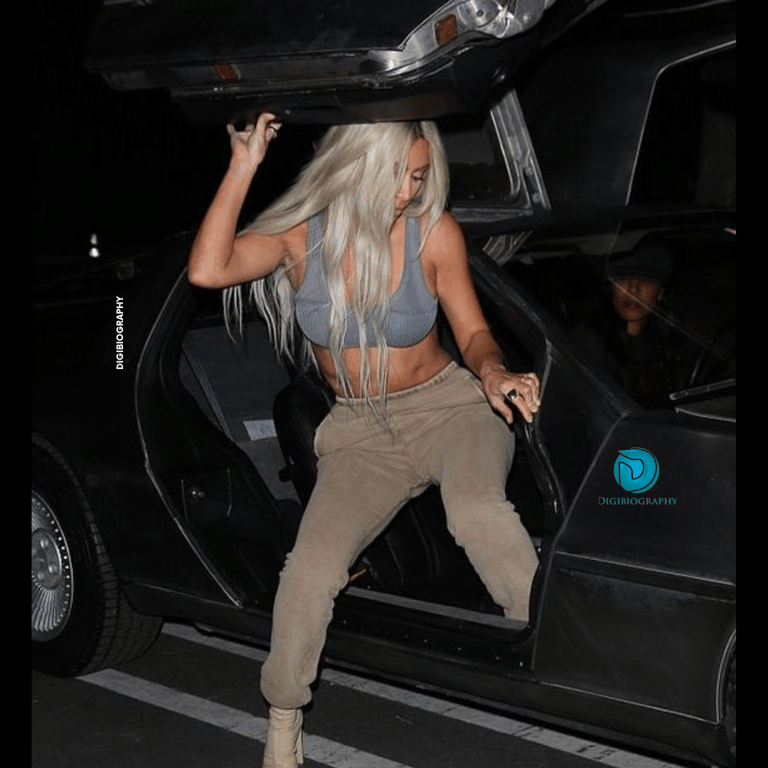 Khloe Kardashian sitting in her tesla car while wearing a blue and grey dress