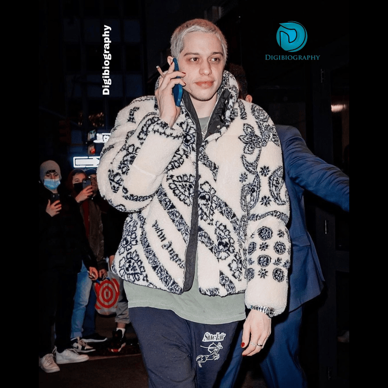 Pete Davidson wearing a jacket and talking on the phone at the street