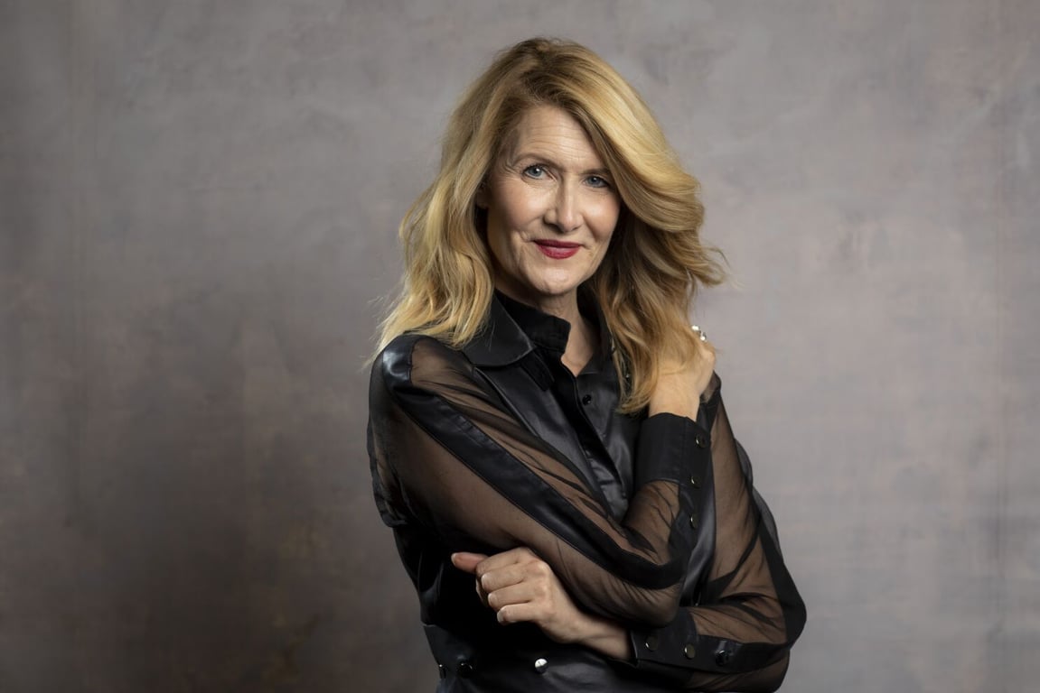 Laura Dern wears a black top and stands in front of the wall