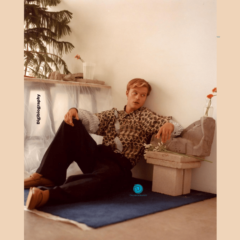 Rudy Pankow sitting in his house on the floor and gives a side pose