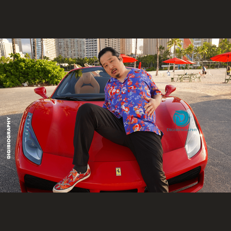 Bobby Lee sitting on her car while wearing a purpal-flawer half shirt and black jeans