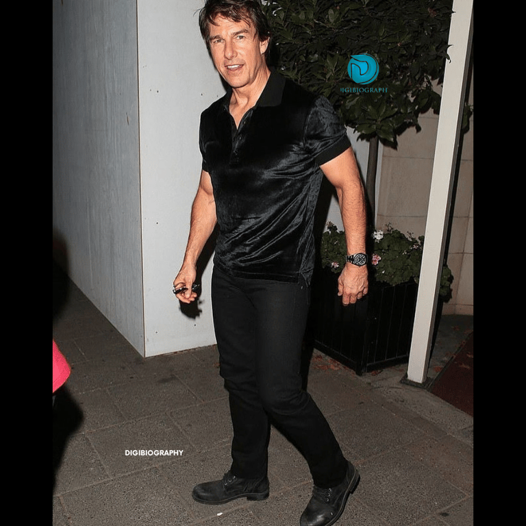 Tom Cruise stands on the floor while wearing a black t-shirt and black jeans