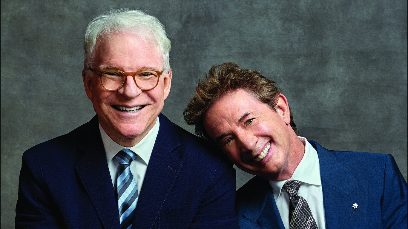 Martin Short sits with Steve Martin in blue suits and both are laughing
