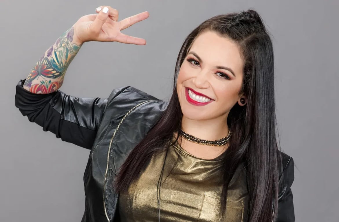 Jacqie Campos wears a black jacket and showing 2 fingure and gives a smile 