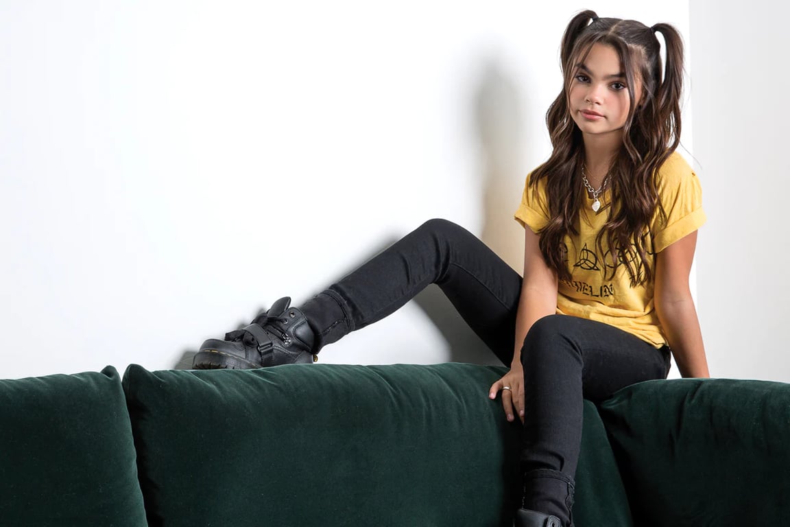 Ariana Greenblatt sitting on the top of the sofa white wearing a yellow and black shoes