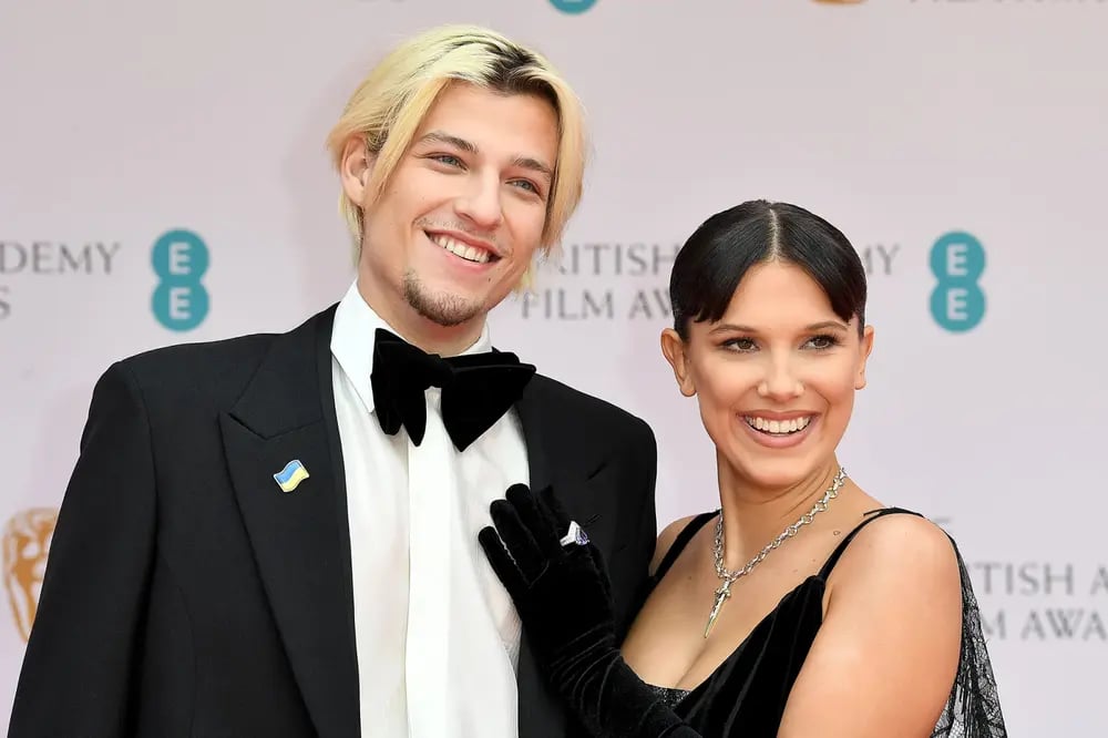 Millie Bobby Brown and Jake Bongiovi both are wearing the same pattern black dress and giving a smile to the media