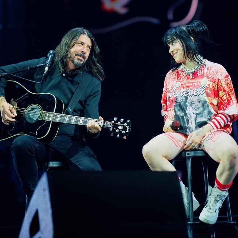 Billie Eilish sitting with a star who is playing guitar on a stage show