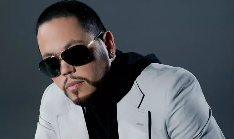 AB Quintanilla in a suit with sunglasses sitting in a studio