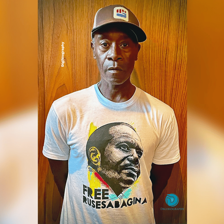 Don Cheadle wears a white t-shirt and cap, stands in their house