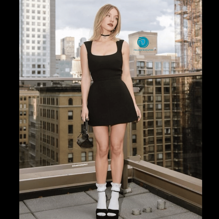 Sydney Sweeney wearing a black dress and stands on the terrace