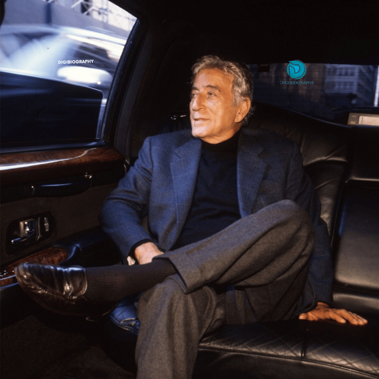 Tony Bennett sitting in her car while wearing a blue coat and black t-shirt