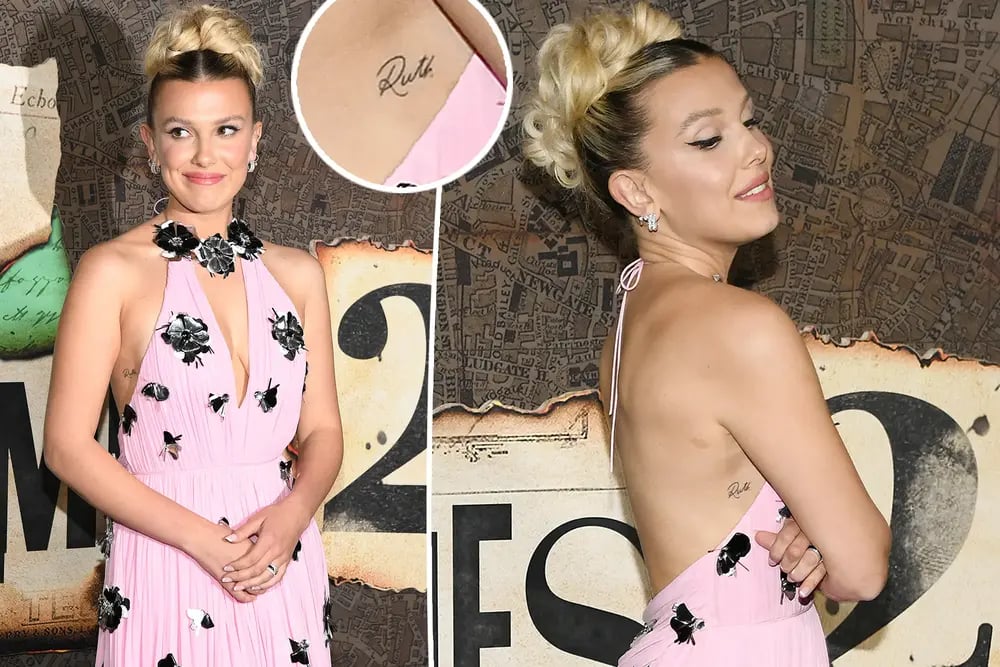 Millie Bobby Brown showing tattoo to the media at a function wearing a pink dress