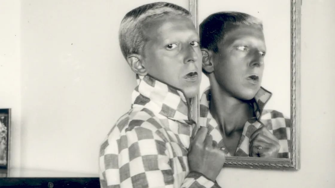 Claude Cahun wear a shirt and stand in front of mirror and gives side pose