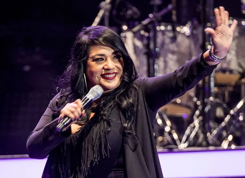 Suzette standing in a stand in black dress holding a mike