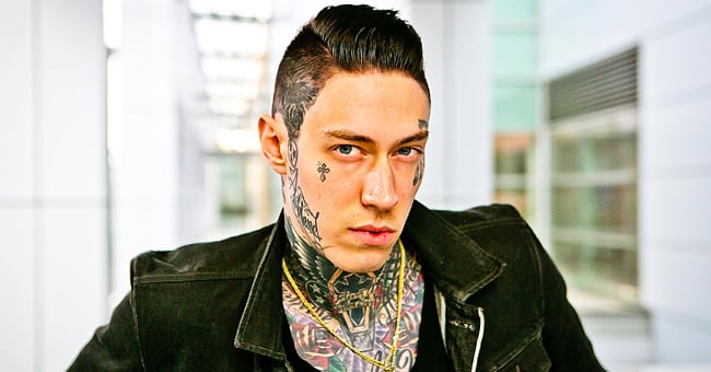 Trace Cyrus wears a black jacket with a golden chain on his neck looked toward the camera
