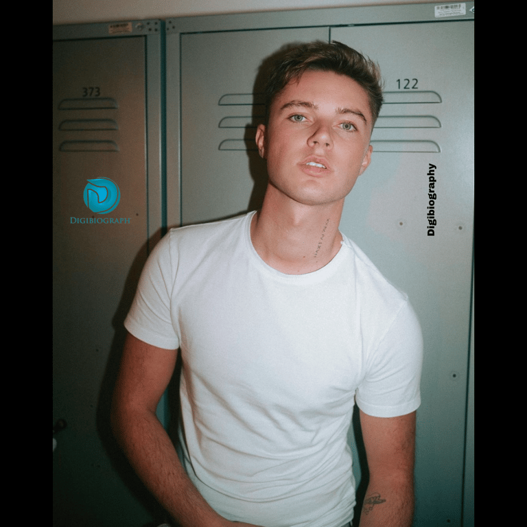 HRVY wears a white t-shirt and stands in front of the locker