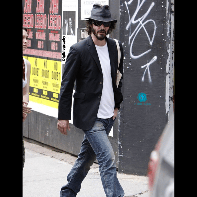 Keanu Reeves wearing a black coat and white t-shirt while walking on street