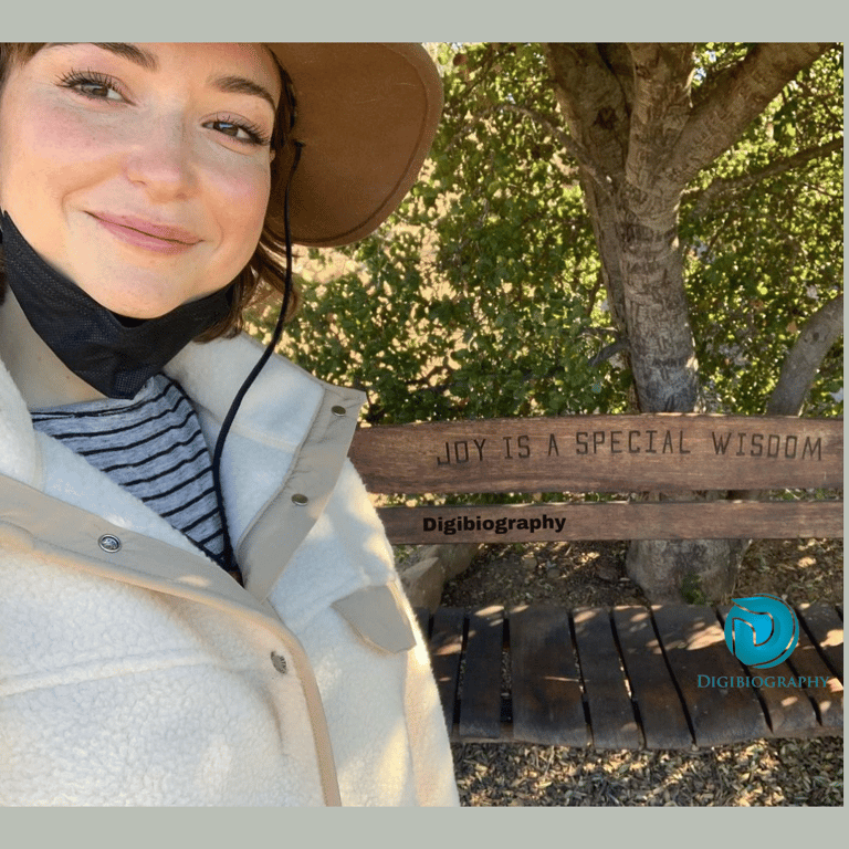 Milana Vayntrub taking a selfie in the forest while wearing a cap and jacket