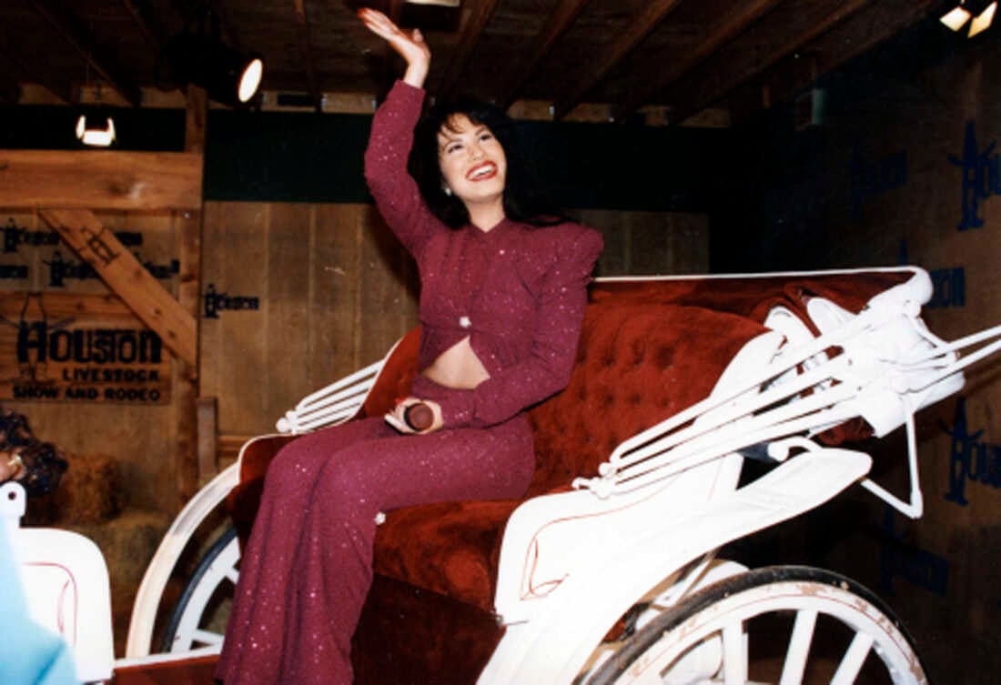 Selena Quintanilla sitting in Horse Carriages saying bye to someone in a red dress