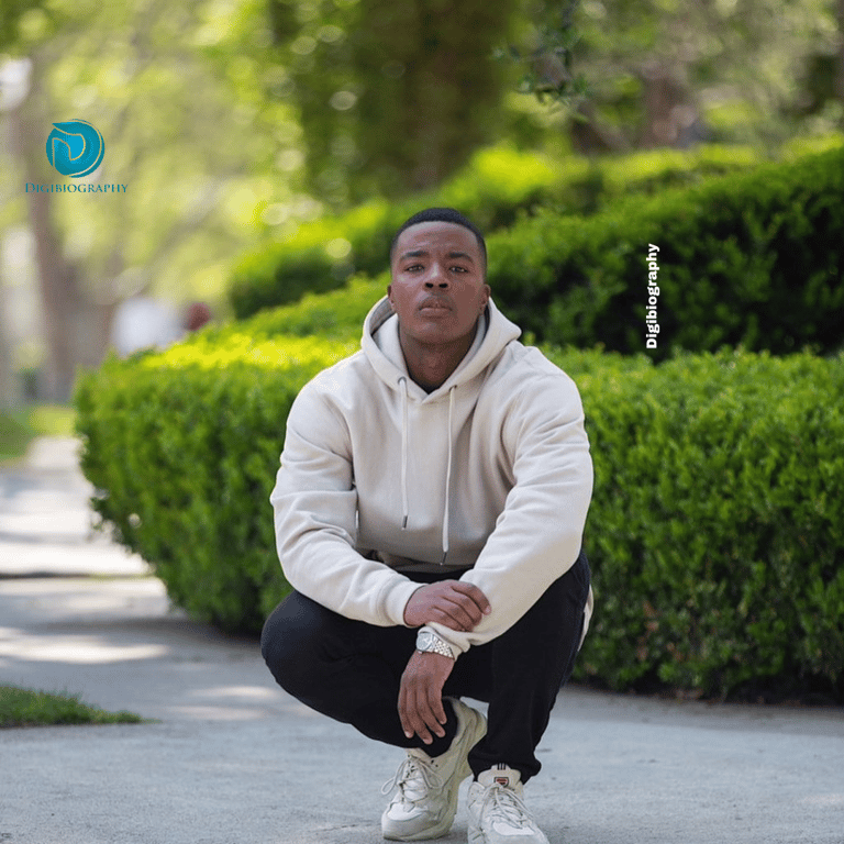 Daniel Ezra sitting in the park, while wearing a white sweatshirt