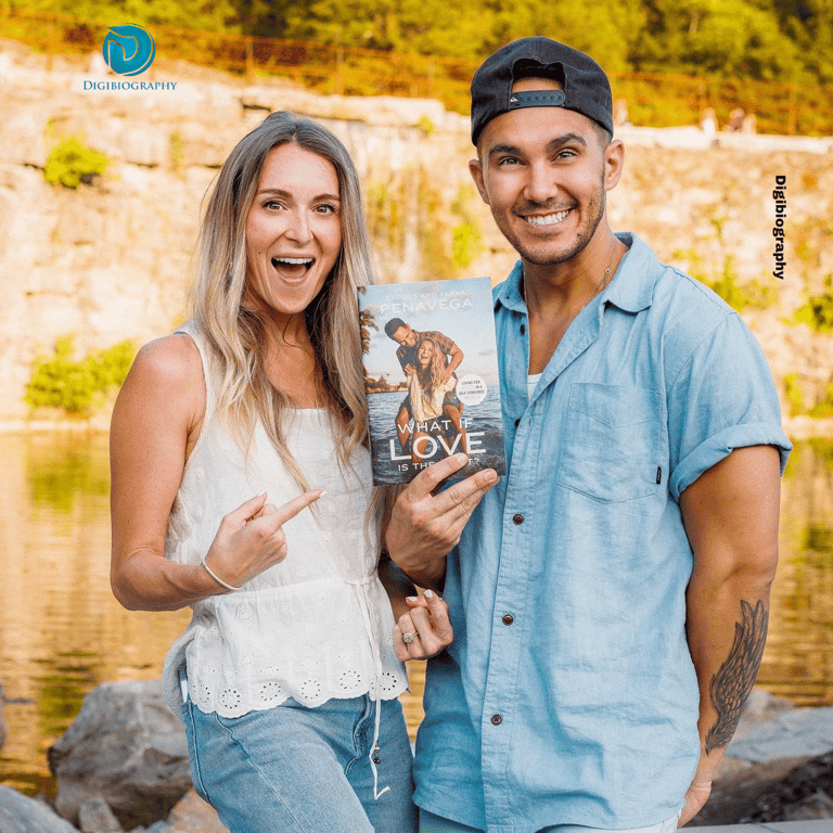 Carlos PenaVega stands with their wife nearby the lake while wearing a blue shirt