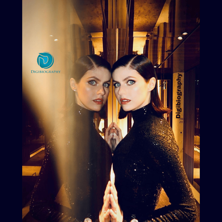 Alexandra Daddario wears a black dress stands very close to the mirror and gives a side pose