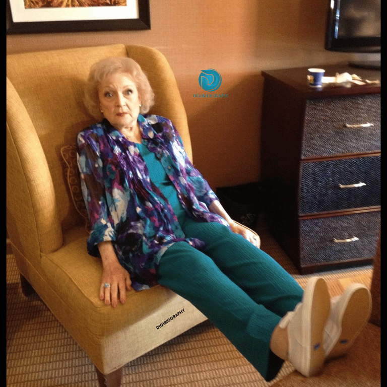 Betty White is sitting on the sofa and wearing a purple follower print shirt