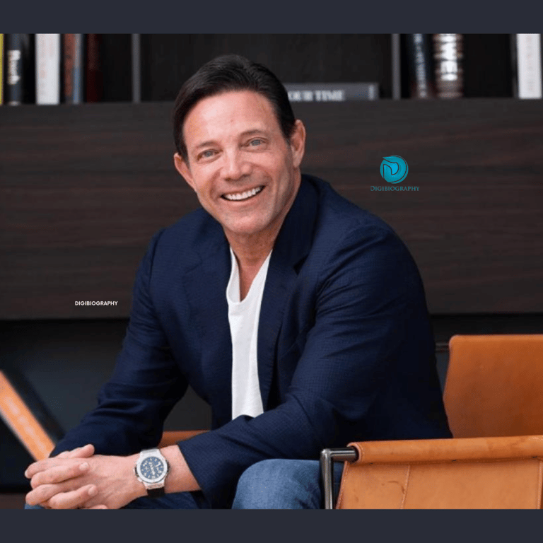 Jordan Belfort wearing a black coat and white t-shirt while sitting on the chair