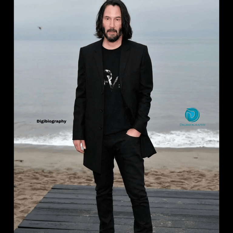 Keanu Reeves wearing a black blazer and black t-shirt while standing on the beach