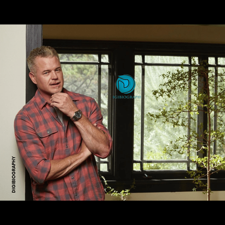 Eric Dane stands close to the wall and wearing a red check shirt