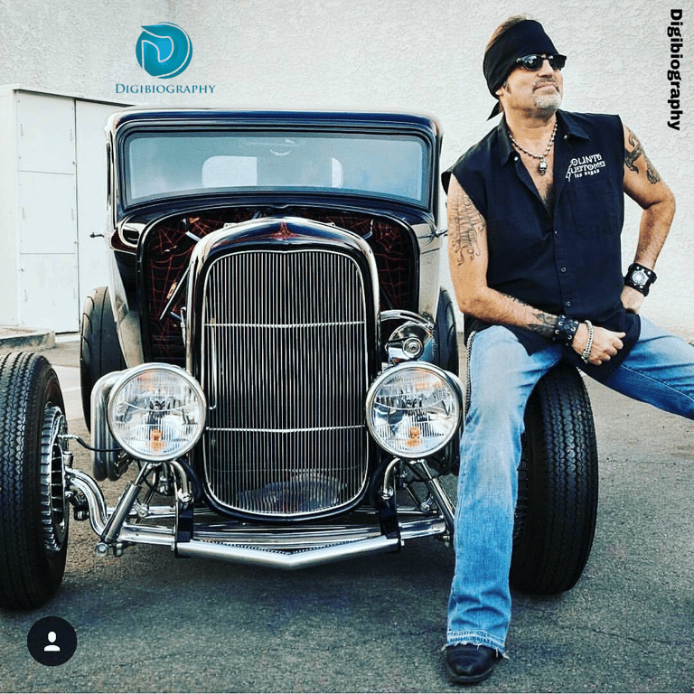 Danny Koker sitting on the first wheel of the black car while wearing a black shirt
