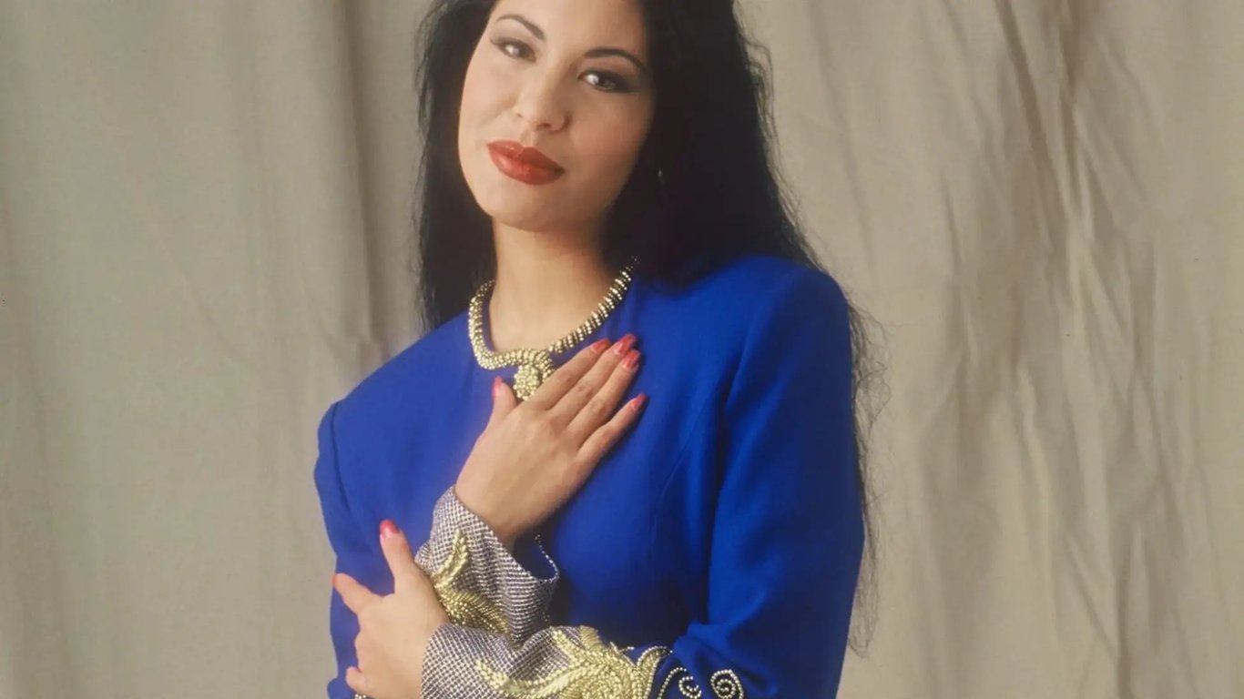 Selena Quintanilla wearing a blue dress holding a hand on their chest