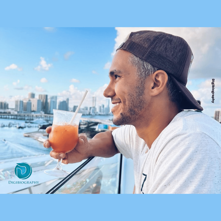 Carlos PenaVega is drinking juice while seeing a view and wearing a white t-shirt