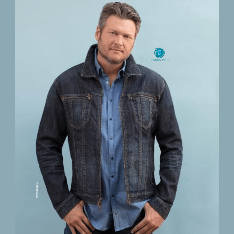 Blake Shelton wearing a blue jacket and standing on the floor