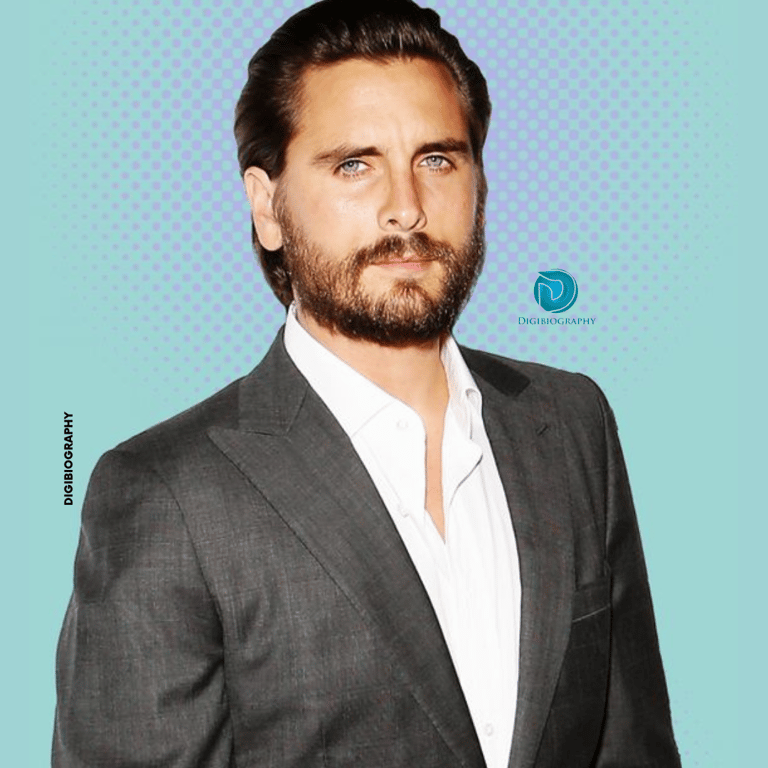 Scott Disick wearing a gray coat and white shirt while standing in blue background