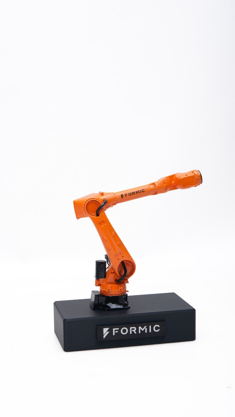 An orange scale model of a Formic robot arm on a black base with the Formic logo