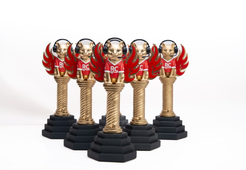 Five gold cat trophies in red RC jerseys and gaming headsets, with red flame wings on black stepped bases