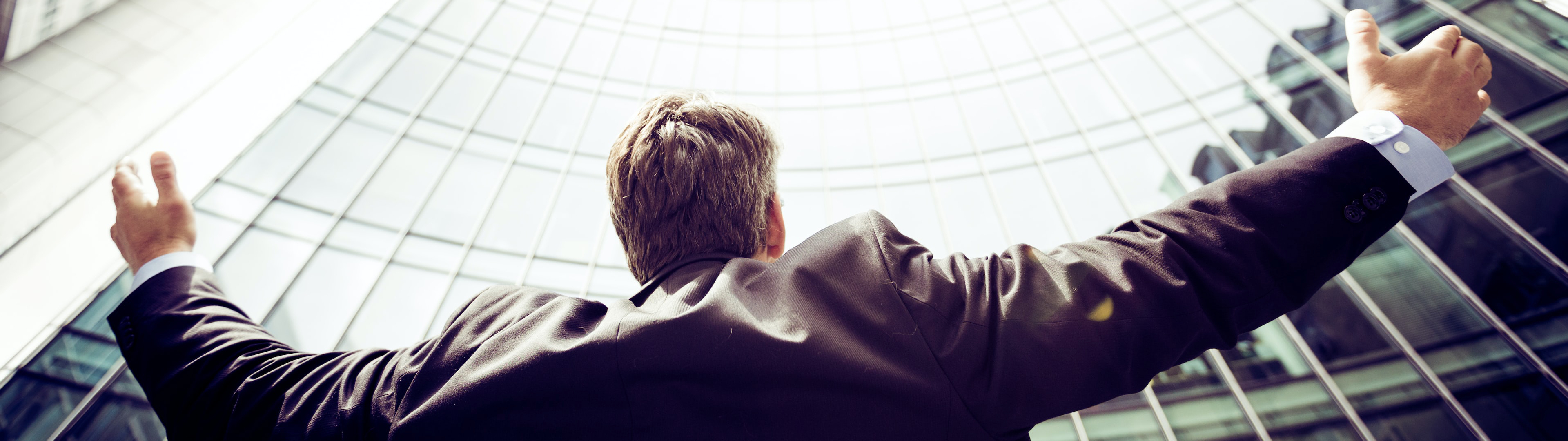 Man with his arm open looking up to a building