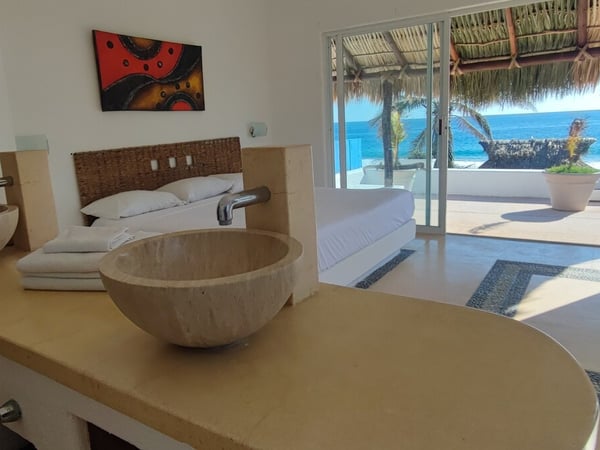 Recámara frente al mar con lavabos de piedra natural y amplia vista a la terraza palapa y el Pacífico