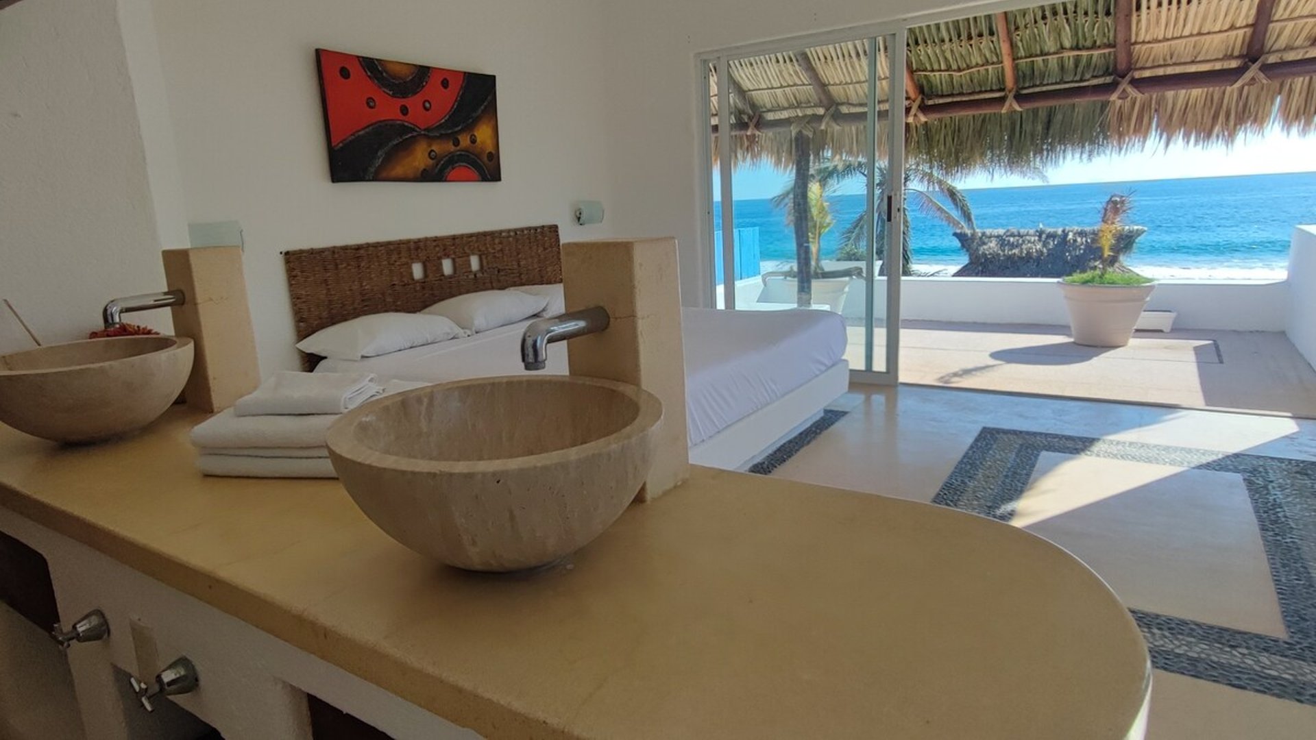 Recámara frente al mar con lavabos de piedra natural y amplia vista a la terraza palapa y el Pacífico