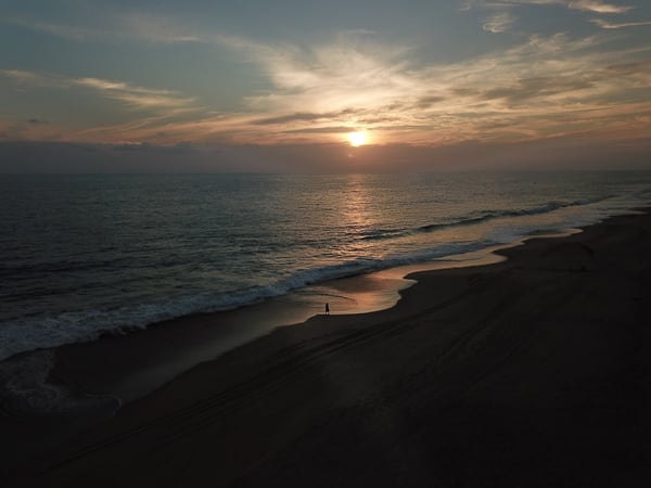 Atardecer aéreo sobre playa desierta del Pacífico con figura solitaria a orillas del mar