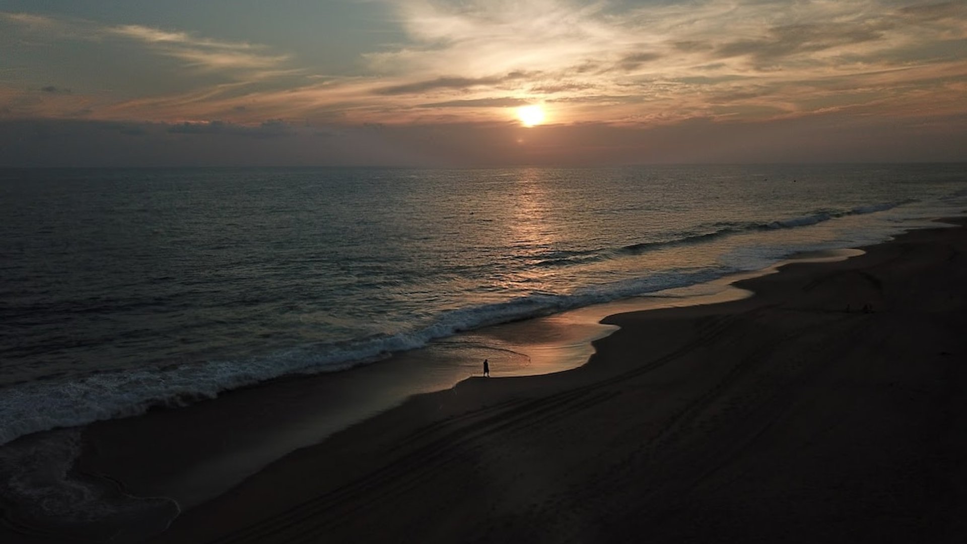 Atardecer aéreo sobre playa desierta del Pacífico con figura solitaria a orillas del mar