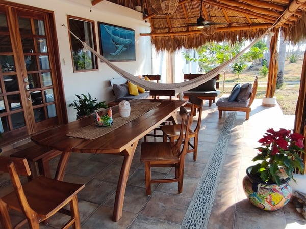 Terraza bajo palapa con mesa de madera, hamaca, sala exterior y maceta talavera en luz natural