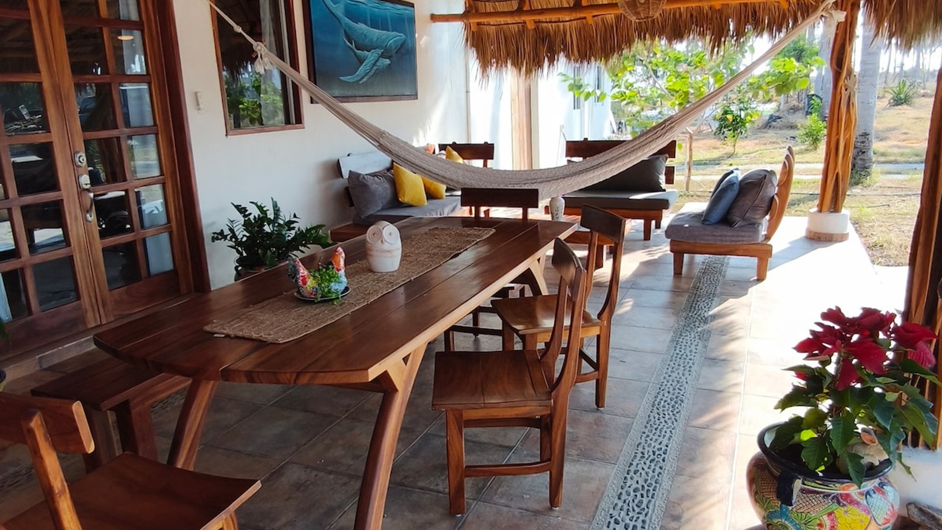 Terraza bajo palapa con mesa de madera, hamaca, sala exterior y maceta talavera en luz natural