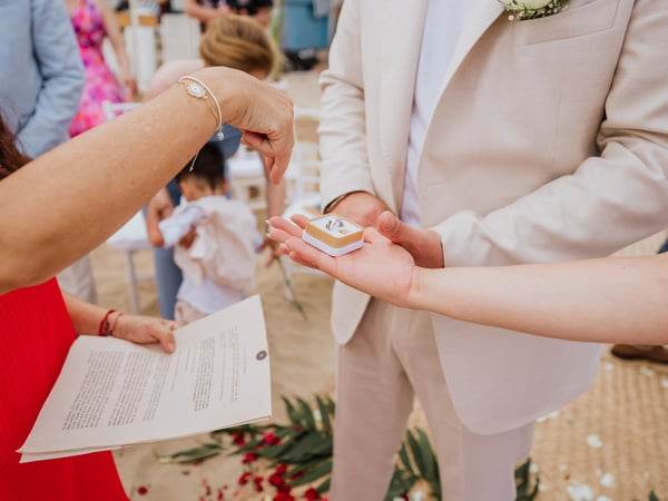 Intercambio de argollas durante ceremonia de boda frente a la playa con invitados al fondo