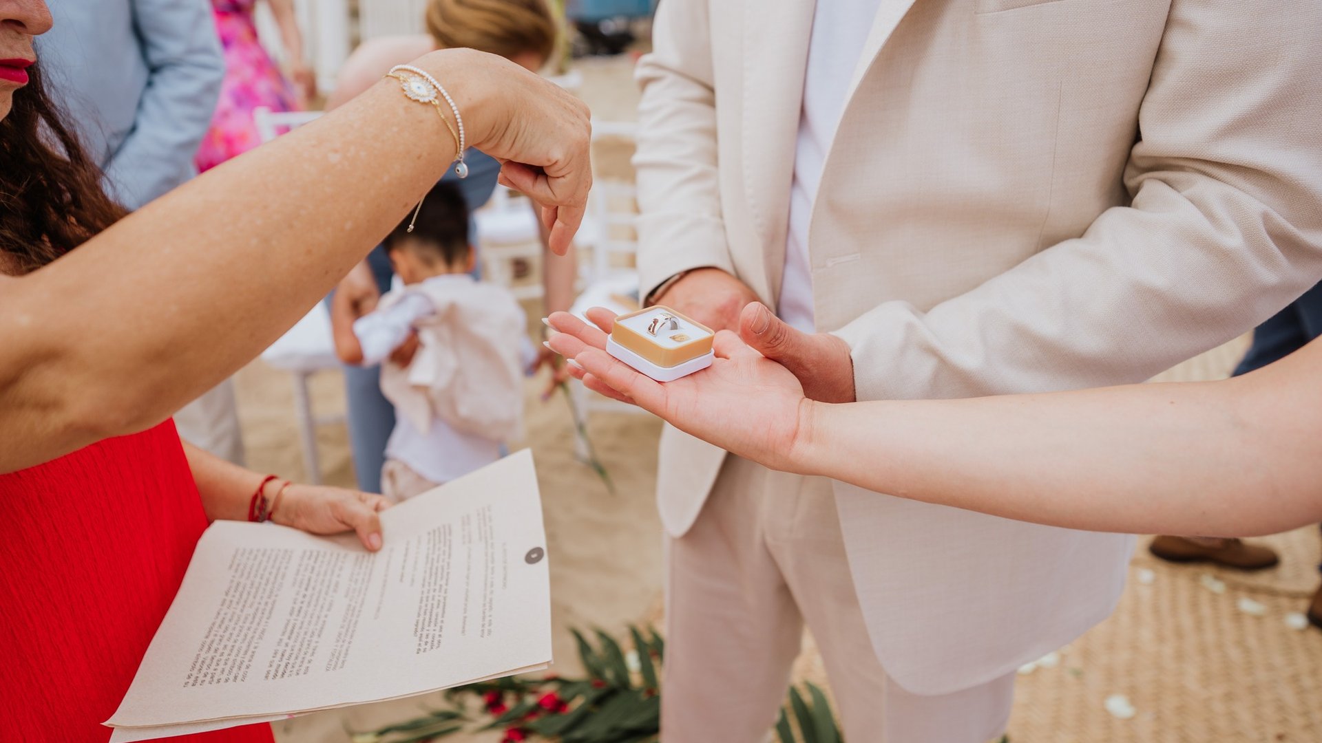 Intercambio de argollas durante ceremonia de boda frente a la playa con invitados al fondo