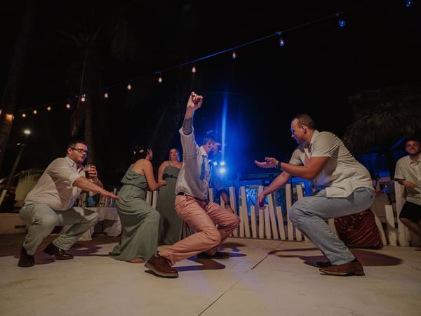 Invitados bailando en pista nocturna con luces colgantes y palmeras de fondo